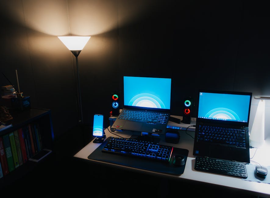 Nighttime office desk setup with laptops, illuminated keyboard, and ambient lighting