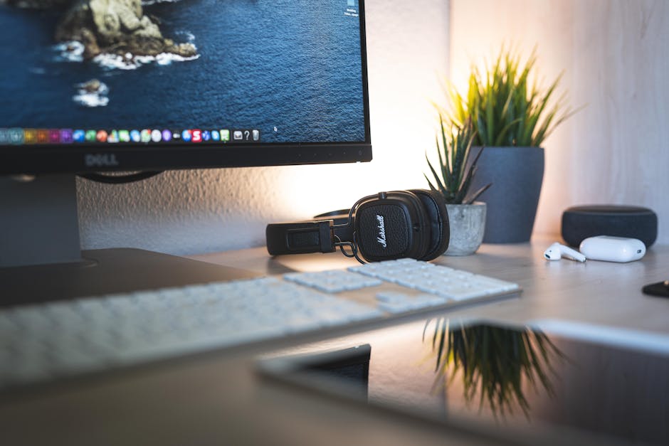 A minimalistic desk setup featuring a monitor, headphones, keyboard, and green plants